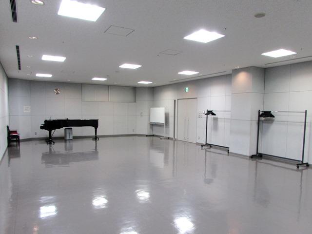 光沢感のある床と白い壁と天井の室内に、黒いピアノが1台設置してある写真