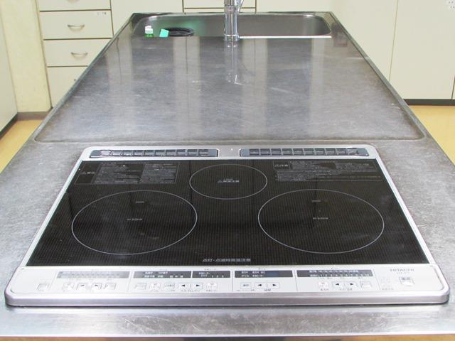 上部に3口の電気コンロと、流しが設置されている調理台の写真
