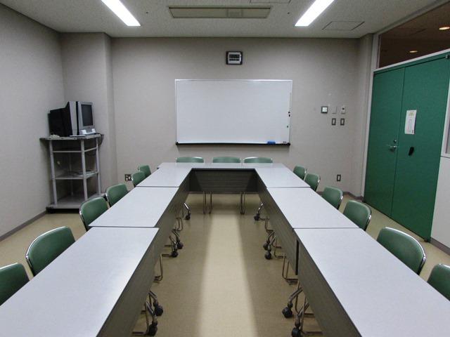 白壁と緑扉の縦長の部屋に、白い長テーブルが向かい合って並べてある写真