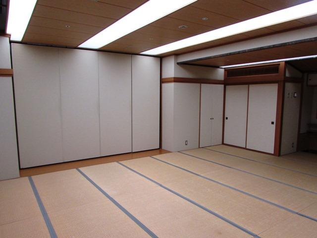 床は畳敷き、天井は木の板と白いカバーのついた蛍光灯が並んでいる。壁は白く、一部は可動式で、取り外すこともできる和室の写真