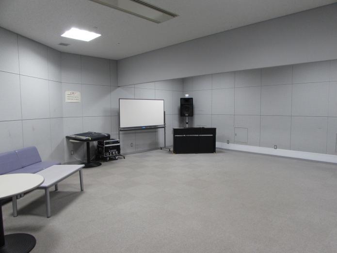 カーペットの敷かれた床に白系統の色で統一されている防音素材の壁と天井の部屋にテーブルやソファ、電子ピアノが置かれている写真