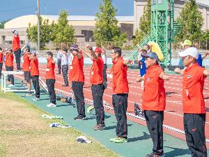 写真：陸上競技場で横一列に並び、両手を大きく左右に伸ばした体操を行うスポーツ推進委員の皆さん