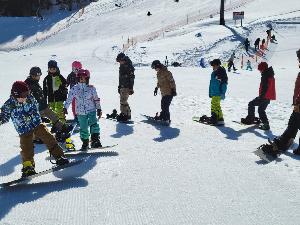 写真：参加者が片足にスノーボードをつけう練習をしています