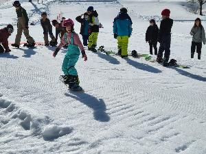 写真：参加者が片足にスノーボードをつけた状態でゲレンデを少しずつ滑っている様子です