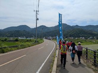 写真：参加者が歩道を歩いています。鯖石の山々が写っています