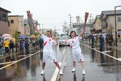 聖火ランナーがトーチを持った手を高く上げて持ってポーズをとっています