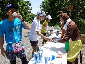 写真：サルの着ぐるみを着たボランティアスタッフと給水をしているランナーが写っています