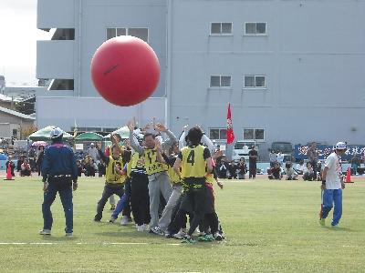 写真：大玉小玉送りで、縦に一列に並んだ競技者の頭上を赤い大玉が転がっていきます