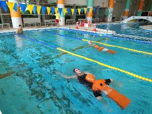 写真：溺者救助・搬送練習用の水難救助訓練人形を抱えながら、プールで背泳ぎしています