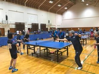 写真：ラージボールの試合の様子。写真右側の男性が手を伸ばし相手に球を打ち返す様子