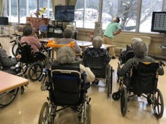 写真：入居者が集まりラジオ体操をする様子。多くの方が車いすに座っています