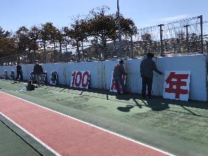 写真：陸上競技場のフェンスに記念パネルを掲出するための準備をしている様子です