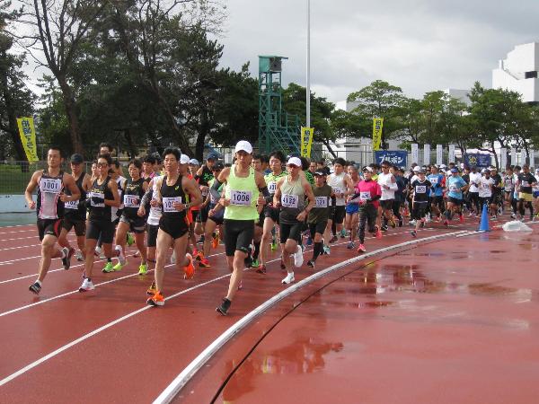 写真：参加者がスタートし陸上競技場を走っている様子です。雨は降っていませんが路面が濡れています。