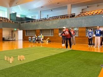 写真：赤のビブスを着た男性がモルックを投球する様子。手前のスキットルに当たりそうです。