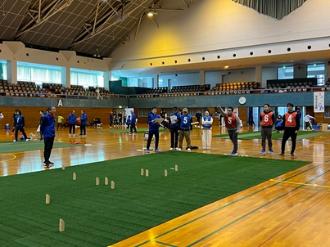 写真：男性が腕を大きく振って投球しています。スキットルがコートの中に散らばっています