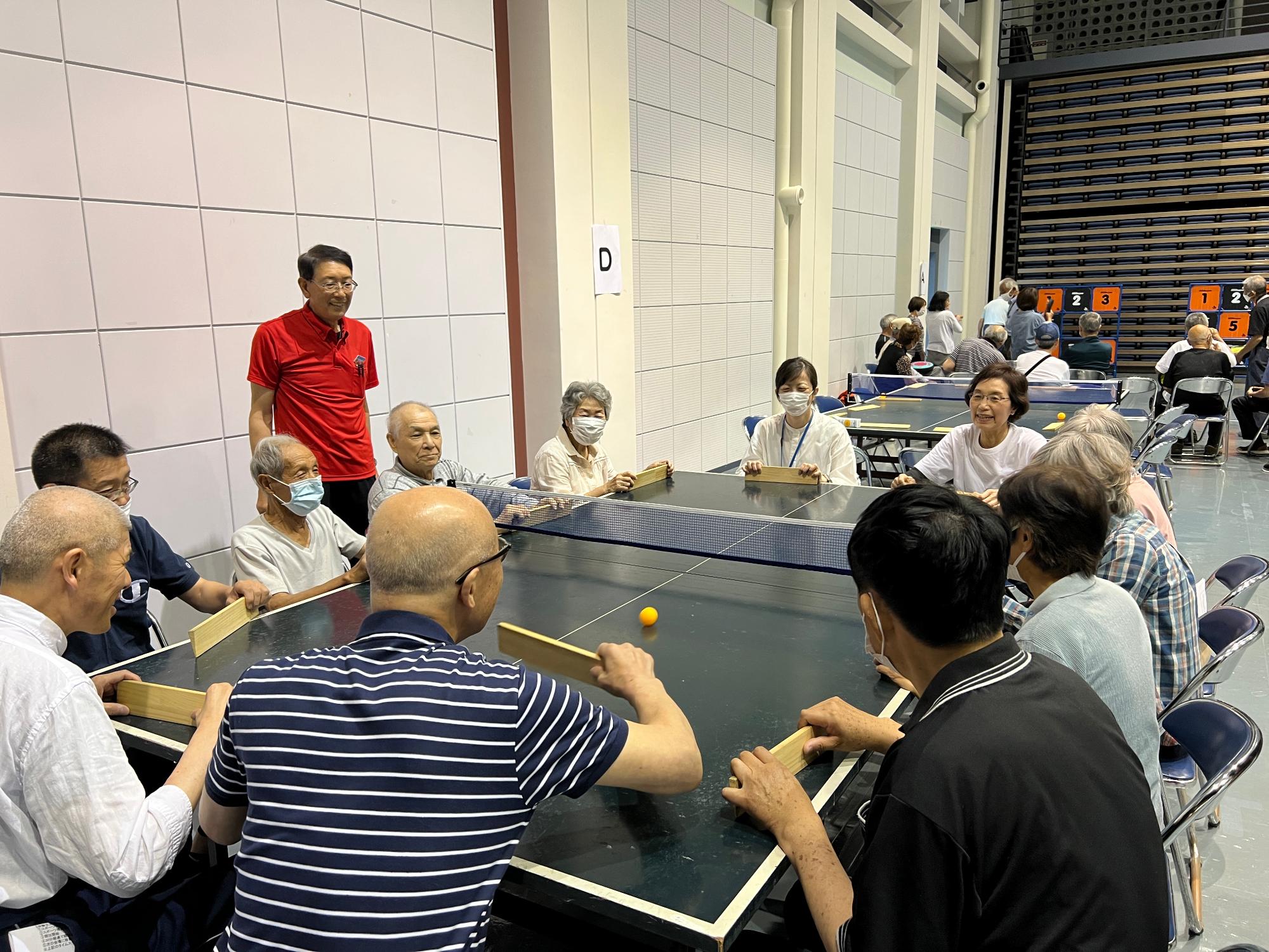 写真：卓球台の周りに座り、総勢12人ほどで卓球バレーを楽しんでいます。