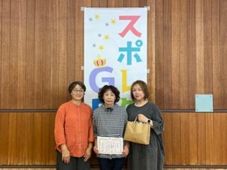 写真：Cブロックで優勝したチーム別山。女性3人がにこやかな表情で写っています。右側の女性は景品を持っています