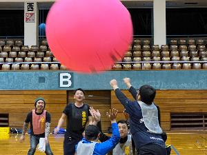 写真：同じ色のメンバーに支えられたキンボールを男性が両手で上に向かってヒットしている様子です