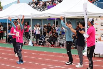 写真：小学生ぱん食い競走の開会セレモニーの様子。大会名誉顧問の黒崎ひろあきさんが紹介されご本人が両手を挙げて応えています