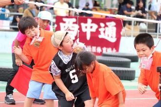 写真：小学生がパンの入った袋の角をかじって取ろうとしています。手を使わず上手に取っています