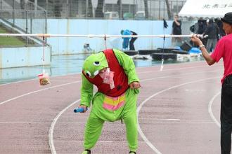 写真：ユーモア賞を受賞した上条地区体協チームの様子。黄緑色の怪獣の子どもの仮装をしてバトンを持ち、パンをくわえようとしています