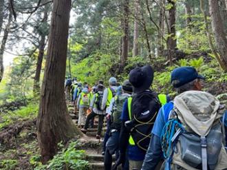 写真：多くの参加者が列になり登山道を歩いています。登山道は階段になっています
