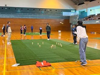 写真：参加者が投げたモルックが勢いよく飛んでいます。周りで他の参加者がどこに当たるか様子を見ています