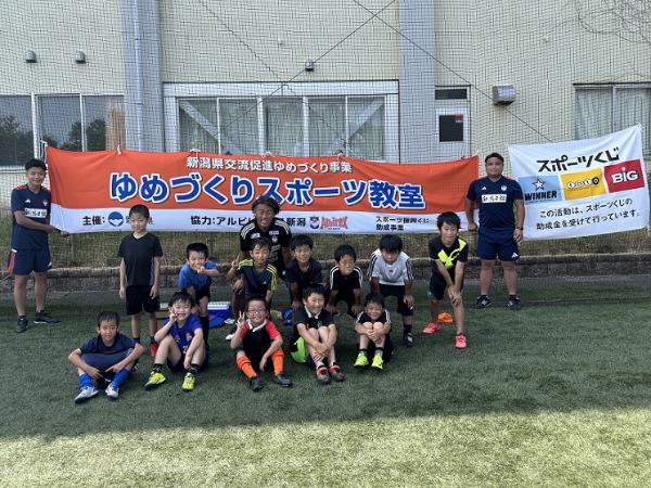 写真：アルビレックス新潟のコーチ3人と参加者が記念撮影をしています。背後にはゆめづくりスポーツ教室と書かれた横看板も写っています