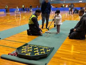 写真:女の子がスカットボールをしています。クラブを持ってスカット台に向かってボールをスティックで打っています