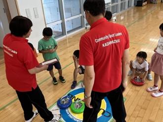 写真：スポーツ推進委員がカローリングの得点つけ方を説明しています。赤いポロシャツを着用しています