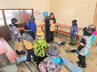 写真：休憩室の中で、内山さんがスノーボードを立てて、参加者にボードの説明をしています