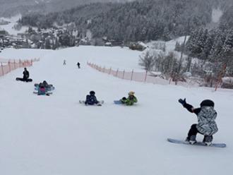 写真：ゲレンデを参加者がスノーボードで滑る練習をしています。他の参加者は順番待ちをしています