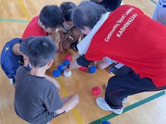 写真：スポーツ推進委員がボッチャの得点つけ方を説明しています。スポーツ推進委員の周りには複数人の児童が話を聞いています
