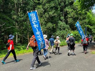 写真：山道を歩く参加者。スポーツ推進員がが市民ウオーキング大会と書かれたのぼりを持って歩いています