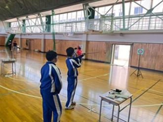 写真：参加者がスポーツ吹き矢を的に向けて狙いを定めています。