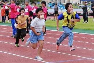 写真：小学生3人が口でしっかりとパンをくわえてゴールを目指して走っています