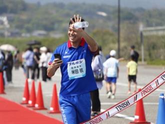 写真：ファンラン招待選手のよねたわたるさんが手を振りながらゴールする様子。にこやかな表情です