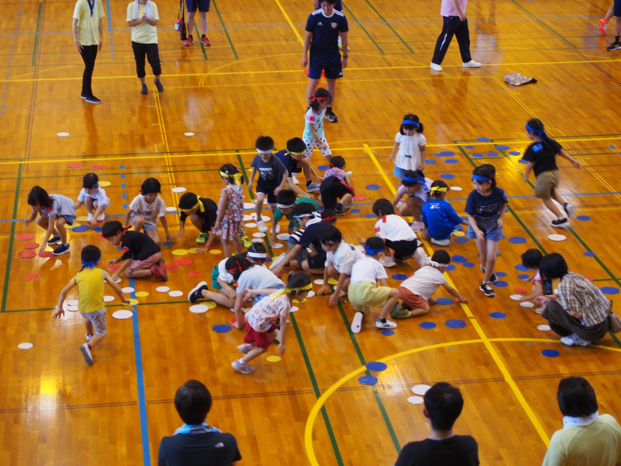 写真：床に不規則に置かれたカードを、自チームの色にひっくり返す遊びをしている子どもたち