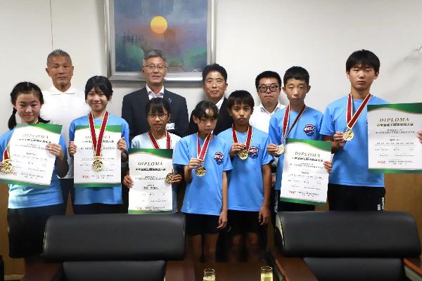 写真：県大会の金メダルを首から下げ、賞状を持つ選手たち。その後ろに桜井市長と指導者3人が並んでいます