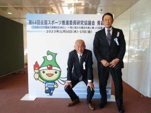 写真：全国スポーツ推進委員連合から表彰を受けた金子さんと曽村さん。表彰式特設パネル前で。