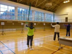 体育館で競技者が的に向かって吹き矢を吹いている写真