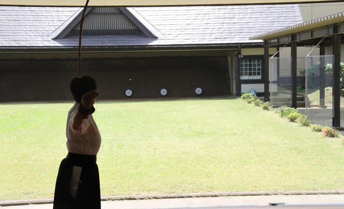 弓道場で弓道着を着た利用者が的に向かって弓を引ている瞬間の写真