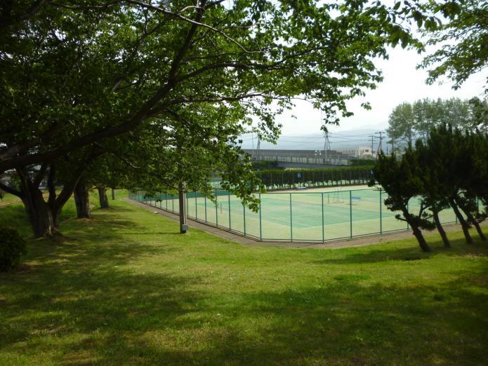 木々の向こうにフェンスに囲まれたテニスコートがある写真