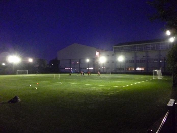 多数の夜間照明で照らしているサッカー場で練習をしている写真