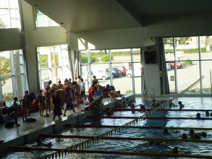 2方向がラス壁になっているプールで大勢の学生たちがコースごとに泳いで練習する様子の写真