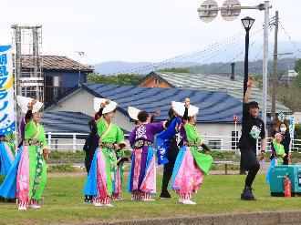 写真：よさこいグループまつりや倶楽部が鳴子を持って踊っています。緑とピンクのきれいな衣装で踊っています