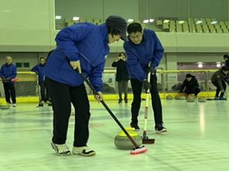 写真：スポーツ推進委員が月例研修会でカーリングをする様子。ストーンの前をブラシではいています