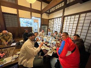 写真：荻ノ島かやぶきの里での食事の様子。囲炉裏の横に置かれた大きなテーブルには所狭しと料理が並び、選手みんなで囲んでいます。