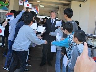 児童たちがセルビア共和国と日本の手持ち旗を持ってグリシッチ氏を歓迎している写真