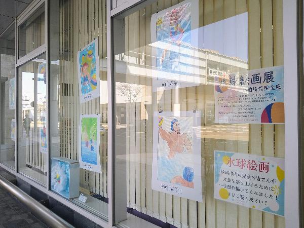 写真：信用金庫の窓ガラスに小学生の水球の絵が展示されています